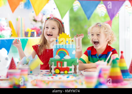 Kids Birthday party. Enfant blowing out candles on cake coloré. Maison décorée avec des bannières drapeau arc-en-ciel, de ballons, de confettis. Les transports et la ferme Banque D'Images