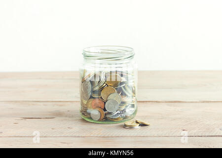 Pièces de monnaie dans un bocal en verre. L'épargne de l'argent gratuit. Pot avec un assortiment de pièces sur une table en bois, copie de l'espace. Banque D'Images