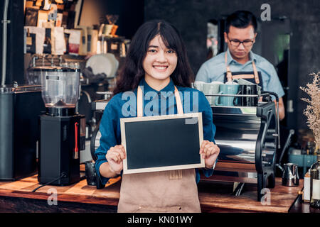 Asian female barista porter jean apron holding blank blackboard menu café au comptoir bar avec collègue avec Smile, cafe service concept,business Banque D'Images