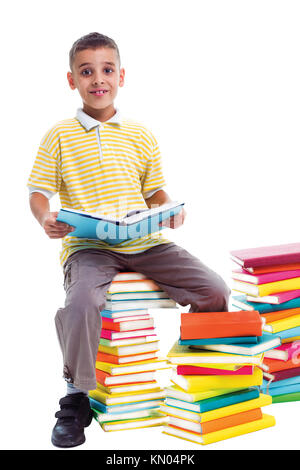 Garçon assis sur une pile de livres et la tenue d'un livre dans ses mains Banque D'Images