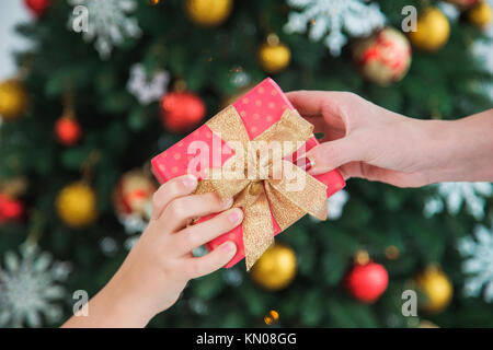 Libre des femelles adultes de part et petite main d'enfant holding Christmas present en rouge du papier d'emballage. Mère et fils ou fille échange présente o Banque D'Images