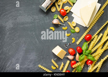 Aliments italiens Concept et design de menu. Mélange de pâtes, fromages, épices, tomates et basilic sur un arrière-plan en ardoise grise. Mise à plat, vue supérieure avec copie espace Banque D'Images