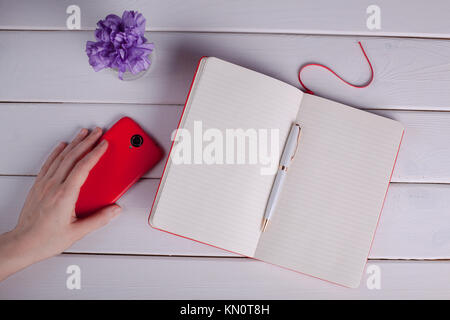 Femme main tenant un smartphone. A proximité se trouve un ordinateur portable avec un stylo. Banque D'Images