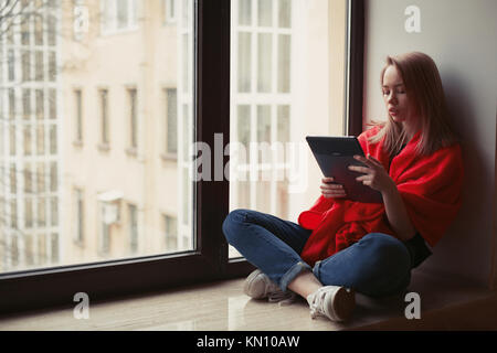 Portrait d'une jeune fille lisant un e-book à la fenêtre. Banque D'Images