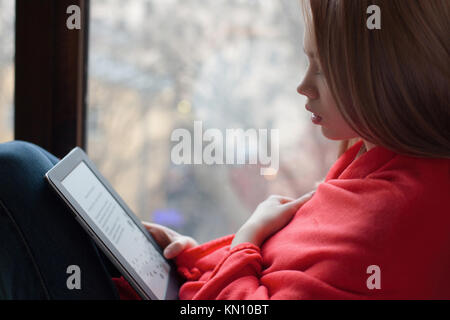 Portrait d'une jeune fille lisant un e-book à la fenêtre. Banque D'Images