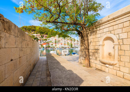 Rue étroite avec de l'eau robinet dans Supetar port avec bateaux de pêche, île de Brac, Croatie Banque D'Images