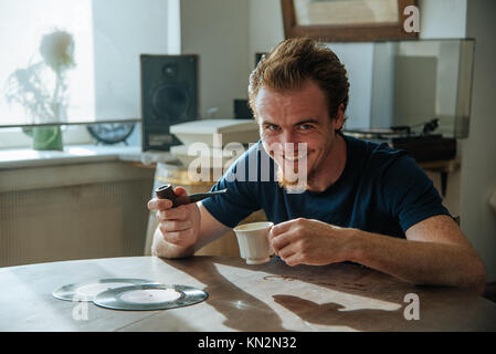 Smiling young man du tuyau de fumée, boire un café, écouter de la musique ancienne tôt le matin et profiter de sa vie Banque D'Images