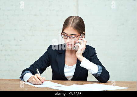 Business Woman talking on phone et la signature de documents à la table in office Banque D'Images