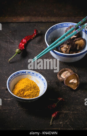 Curcuma poudre et les champignons shiitake dans des bols en porcelaine, servi avec Red Hot Chili Peppers et baguettes turquoise foncé sur table. Voir la série Banque D'Images