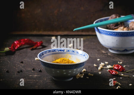 Curcuma poudre et les champignons shiitake dans des bols en porcelaine, servi avec Red Hot Chili Peppers et baguettes turquoise foncé sur table. Voir la série Banque D'Images