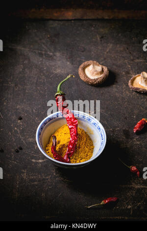 Curcuma en poudre dans un bol en porcelaine, servi avec des champignons shiitake et Red Hot Chili Peppers sur tableau noir. Banque D'Images