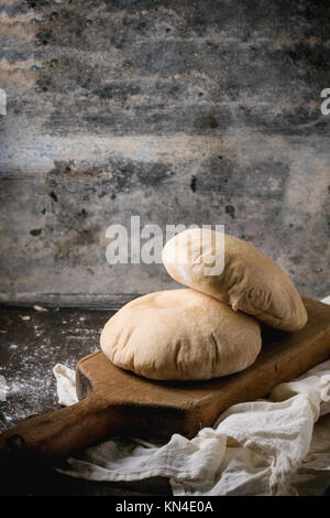 Deux de farine de pain de pita sur planche à découper en bois, servi avec de la farine sur la table sombre Banque D'Images