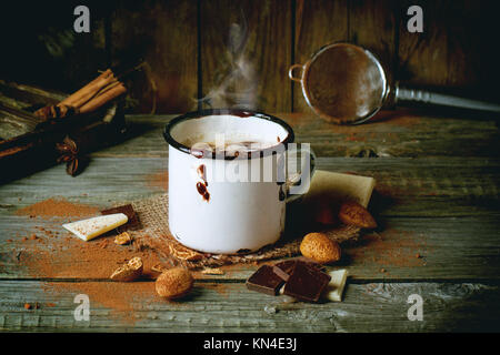 Mug vintage avec du chocolat chaud servi avec des morceaux de chocolat blanc et noir et d'amandes sur la vieille table en bois Banque D'Images