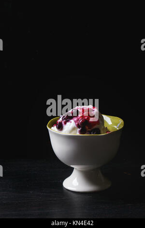 Vase en céramique blanc avec glace vanille, servi avec mélange de fruits rouges sur le tableau noir Banque D'Images