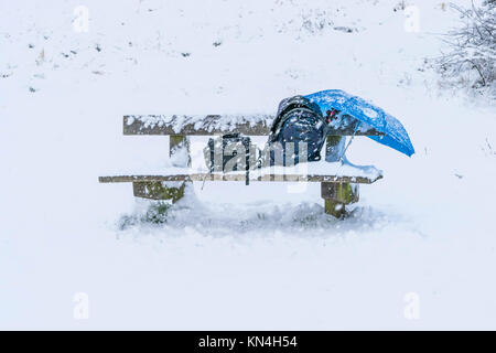 Banc en bois chaise dans un parc couvrir complètement avec de la neige après une tempête de neige pendant l'hiver, vacances de Noël, un sac à dos, parapluie, Sac trépied de l'appareil photo et un petit sac sur la chaise. Banque D'Images