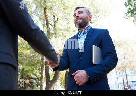 Low angle portrait of mature businessman shaking hands with barbu partenaire méconnaissable à l'extérieur du parc en réunion Banque D'Images