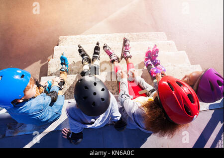 Angle de vue haute de quatre enfants dans les casques et les patins à roues alignées, assis sur l'escalier extérieur Banque D'Images