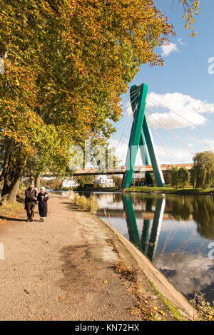 Vieil Homme et femme marche le long de la rivière Brda dans la ville polonaise de Bydgoszcz Pologne avec le pont de l'université derrière à l'automne Banque D'Images