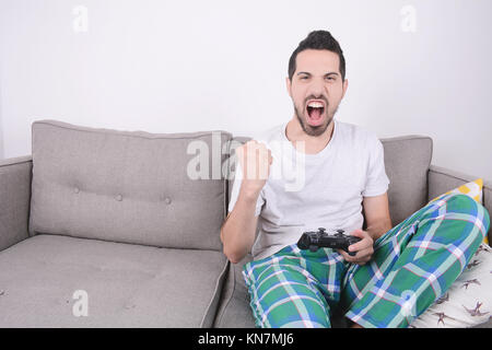 Portrait of young man playing videogames et assis sur la table. À l'intérieur. Banque D'Images