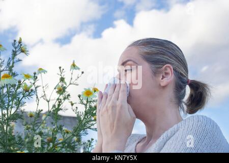 Jeune femme éternuements dans une prairie de fleurs Daisy. Elle est allergique aux fleurs.