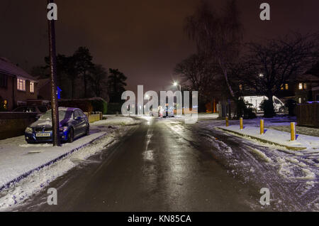 Une rue de banlieue vu la nuit après une journée de neige qui a laissé les trottoirs couverts de neige mais la route a disparu. Banque D'Images