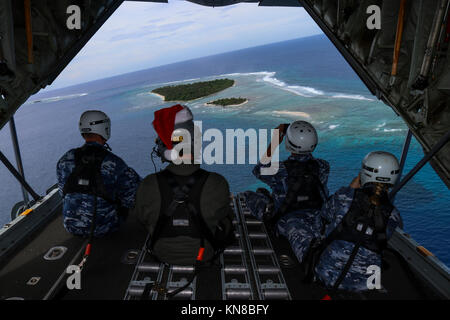 Aviateurs avec la Royal Australian Air Force s'asseoir sur la rampe d'un RAAF C-130J Super Hercules comme il passe par une île micronésienne lors de la 66e opération arbre de Noël 10 décembre 2017 baisse. Chaque année en décembre Américaines et Australiennes C-130 Hercules par hélicoptère de la nourriture, des fournitures et des jouets pour les insulaires dans toute la Micronésie. Banque D'Images