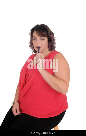 Une belle grande femme dans un chemisier rouge assis sur une chaise avec son stylo dans sa bouche, la pensée, l'isolée pour fond blanc Banque D'Images