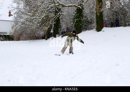 Les enfants et les adultes bénéficiant d'une forte chute de neige par le snowboard et la luge en bas de la colline en vif des champs, Hemel Hempstead, Hertfordshire Banque D'Images