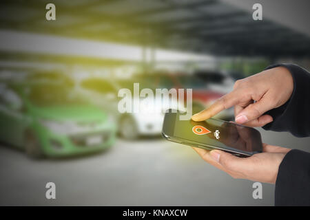 'Car Finder' main femelle useing téléphone mobile contre l'arrière-plan du parc automobile Banque D'Images