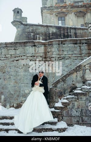 Marié est l'étreindre tendrement belle mariée en étant debout sur les escaliers enneigés de la vieille maison. Banque D'Images