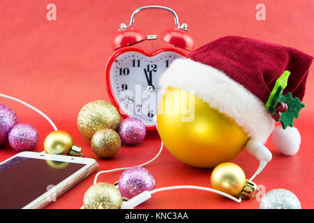 Boule de Noël avec Santa's hat, smartphone avec écouteurs et le réveil, sur rouge Banque D'Images