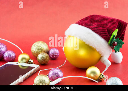 Boule de Noël avec Santa's hat et smartphone avec écouteurs, sur rouge avec copie-space Banque D'Images