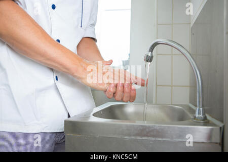 Beau cuisinier, se laver les mains en cuisine commerciale Banque D'Images