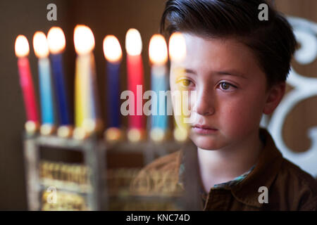 Joli petit garçon juif avec style Pompadour marron du regard et méditant sur Hanoucca bougies dans une menorah d'or pendant la fête des lumières fête des lumières Banque D'Images