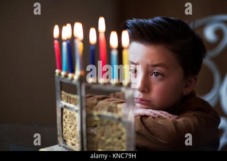 Joli petit garçon juif avec style Pompadour marron du regard et méditant sur Hanoucca bougies dans une menorah d'or pendant la fête des lumières fête des lumières Banque D'Images