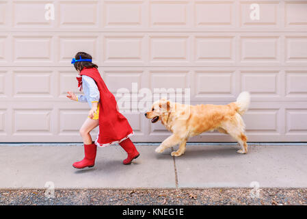 Fille habillée comme un super-héros courant devant une porte de garage avec son chien Banque D'Images