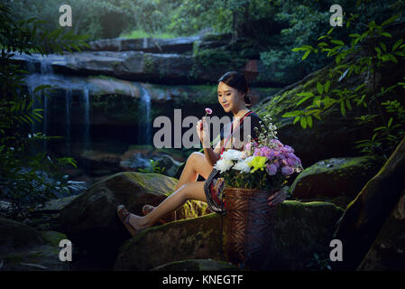 Femme assise avec un panier de fleurs en forêt portant des vêtements traditionnels de la tribu Hmong, Laos Banque D'Images