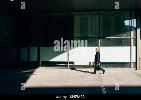 Mature businessman walking outdoors, exerçant son casque de moto, side view Banque D'Images