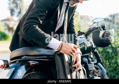 Mature businessman outdoors, penchées sur moto, fait-sac, mid section Banque D'Images