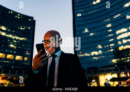 Mature businessman à l'extérieur, la nuit, using smartphone Banque D'Images