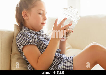 Jeune fille, relaxing on sofa, holding pot d'argent, pensive expression Banque D'Images