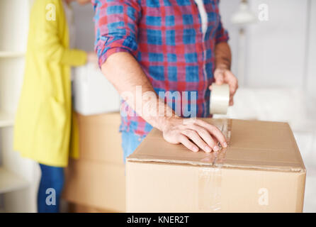 Jeune couple déménager, young man taping up boîte carton, mid section Banque D'Images