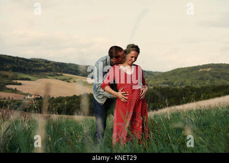 Homme romantique avec les mains sur le ventre de femme enceinte en mode paysage Banque D'Images