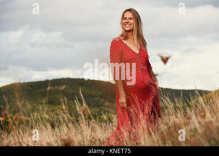 Portrait of happy pregnant woman in red dress on hillside Banque D'Images