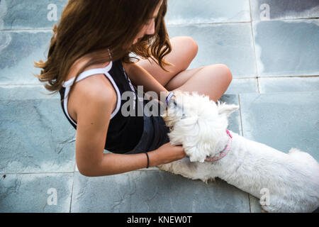 Teenage girl sitting on patio étage petting dog Banque D'Images