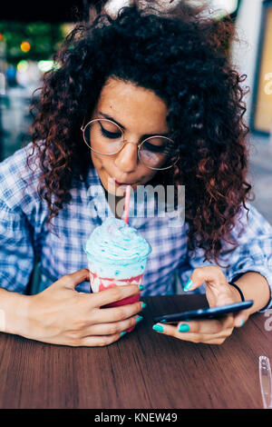 Woman using mobile phone tout en appréciant un verre de glace Banque D'Images