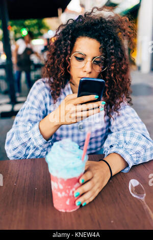 Woman using mobile phone tout en appréciant un verre de glace Banque D'Images