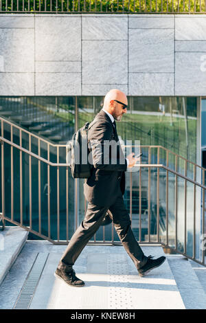 Mature businessman walking outdoors, using smartphone Banque D'Images