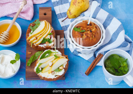 Des sandwichs avec du fromage cottage, de miel, de poire, de noix et de petits gâteaux au chocolat avec du thé à la menthe. Petit-déjeuner festif sain européenne concept. Banque D'Images