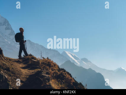 Jeune femme debout avec sac à dos sur la colline et à la recherche sur les montagnes. Paysage avec girl, chemin, montagne, ciel bleu avec des nuages bas au lever du soleil dans N Banque D'Images